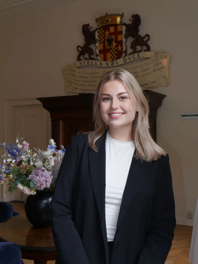 Sanne van der Hoorn staat voor een schouw met wapenschild en een boeket